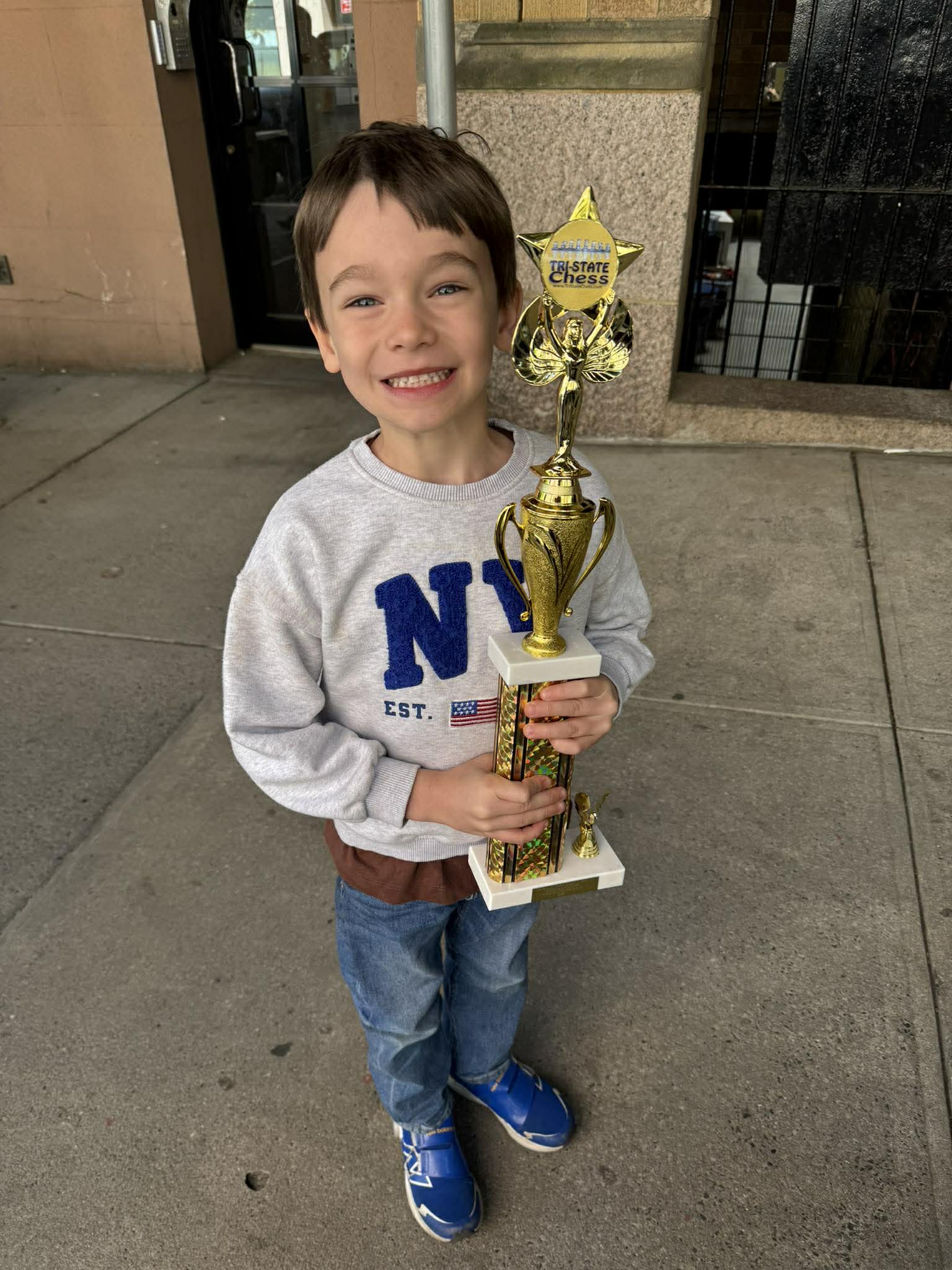 Child holding a first chess trophy after a tournament in NYC