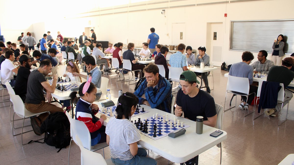 Wide tournament hall with students and families playing chess