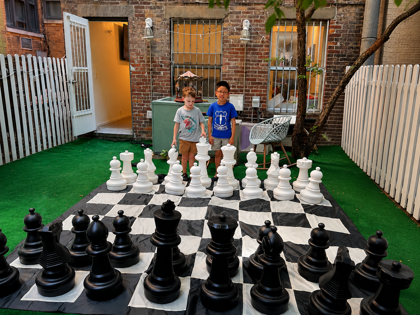 Children playing giant outdoor chess on a life-size chessboard at Chess Max Academy in New York City.