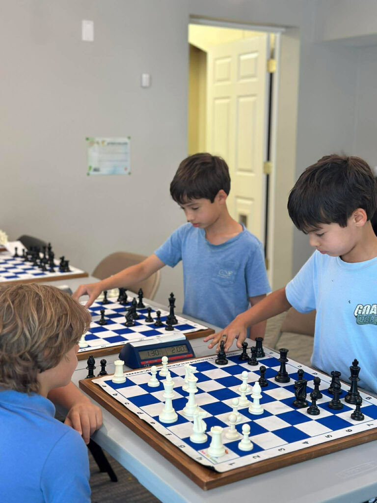 Three students playing chess together at Chess Max Academy